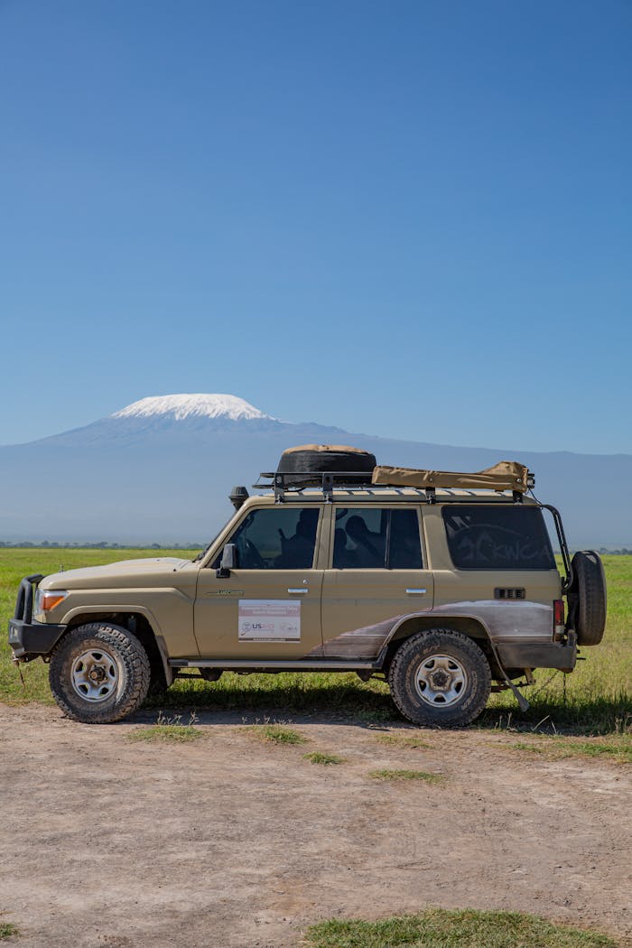 An off-road vehicle parked on a dirt road with Mount Kilimanjaro in the background under a clear sky.