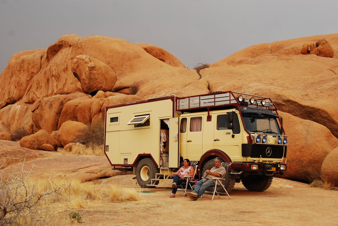 A campervan parked in Namibia's arid desert terrain with two adults relaxing outside.